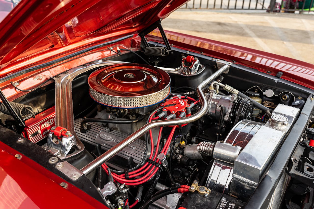 High-resolution image of a classic car engine with hood open, showcasing engine parts and chrome details.